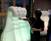 A woman standing in the Pervasive Media Studio, reaching out to touch a large glowing inflatable robot