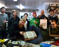 The Canute team posing for the camera with a partially assembled Canute Mk8 and glasses of whisky in a busy workshop.