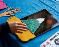 A child's hand using the Bear Abouts paper sensors on an iPad