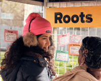 Play:Disrupt Creative High Streets Project, two people outside looking at note cards under an orange sign saying 'roots'