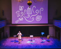 Performer on stage with drawings projected on a screen above