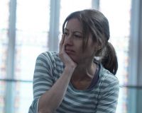 An image of Holly Thomas, a white women, wearing a striped blue and white t-shirt, with shoulder length hair, looking pensive into the distance.