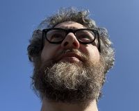 A hairy man's head staring into the distance with blue sky behind