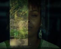 A faded image of a black woman with silver earrings and in traditional Somali dress superimposed onto the entrance of a dark building looking out onto plants and trees.