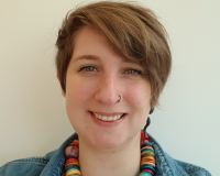 white women with short brown hair. Wearing a denim shirt and multi-coloured necklace.