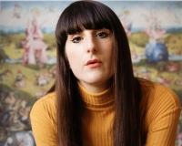 Picture of a woman with brown hair and a fringe, and a yellow jumper. 