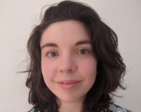 A headshot of a young white woman with shoulder length brown hair in a floral shirt. 