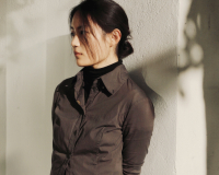 East Asian female leaning against white wall under shades of trees