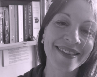 Black and white photo of dark haired white woman smiling with bookshelf behind her