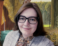 A picture of a smiling woman with shoulder-length brown hair and black glasses. The background is a still image of a forest from the animated Disney Film Sleeping Beauty.