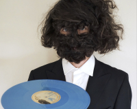 Image of Craig Scott with a hairy face holding a blue record. 
