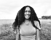 A black and white head and shoulders shot of Natalie who is looking at the camera smiling.
