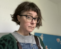 woman with glasses and short hair looking uncomfortable about having a photo taken wearing a green cardigan