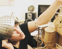 In this picture you can see Leigh Davies sat with a metal collander on his head, handling one of his interactive cardboard sound sculptures from the Playces series.
