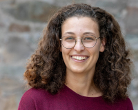 A head-and-shoulders photo of Julia, a white woman with brown curly hair, glasses, laughing, and wearing a red top.