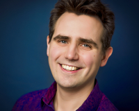 White male with short brown hair, smiling in a purple shirt on a blue background