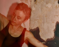 A young woman with a pixie cut pictured mid-dance with airplane-arms