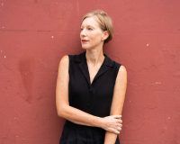 Jo stands in front of a red brown wall.