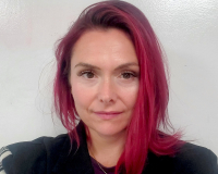 Headshot of Naomi Smyth, a woman with long red hair and a black jacket