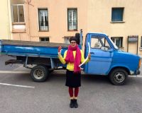 An image of Becca wearing a pink scarf and yellow jumper by a blue van with a cute dog in the drivers seat