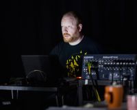 Tim sits in the dark lit only by a laptop screen, looking ghostly