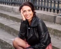 smily women with dark hair and leather jacket in her forties sitting outdoors on concrete steps