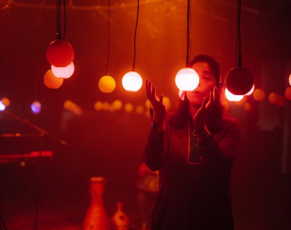 Person stands beside hanging light bulbs and sings