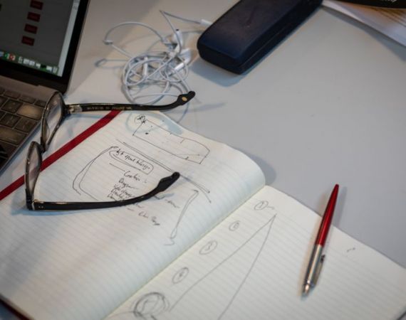 A scene of a desk, with notebook, pen, laptop and glasses