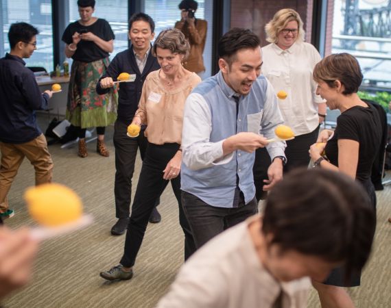 Several people playing together in a room, with lemons balanced on sticks