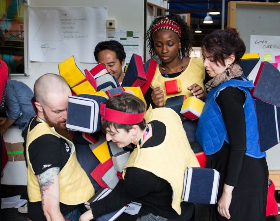 5 people playing a game together that involves multi coloured velcro blocks that stick to their bodies