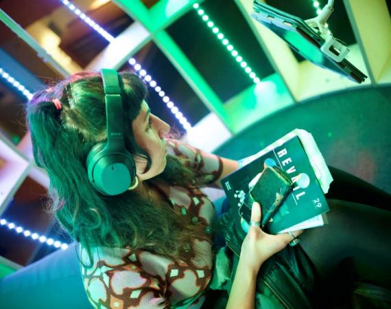 A person sits inside the colourful Joey Pod, wearing headphones and holding their phone