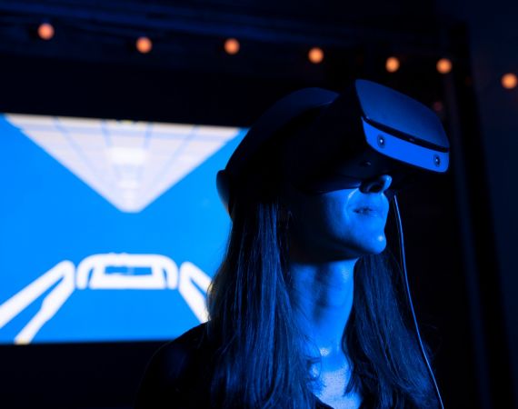Image of a woman wearing a VR headset with the image of a hospital bed projected in the background