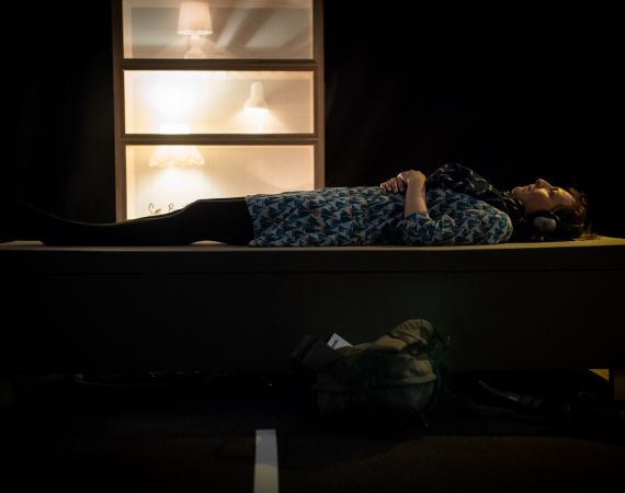 Woman lying down on a platform. Lamps glowing behind. Image by Jon Aitken 