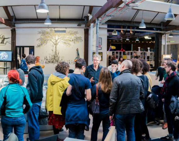 People gathered in a group and talking. In the background there is a black and white illustration on the wall