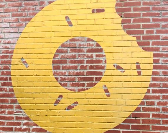 An image of a spray painted yellow doughnut on a brick wall