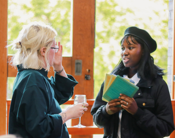 Photo of two people talking at Pervasive Media Studio. One is holding a glass of wine, the other is holding some zines