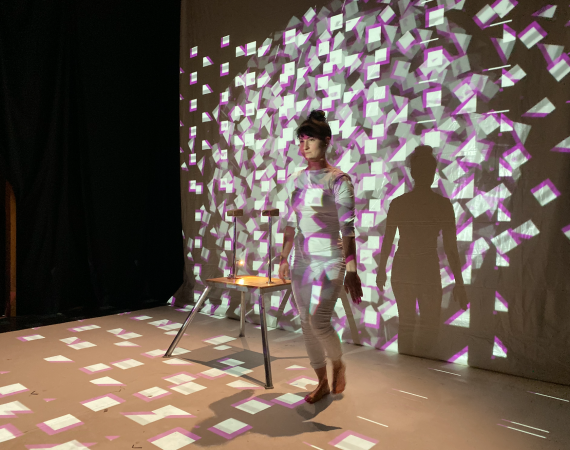 Photo of a person stood in front of a screen with a projected image on their body and the screen