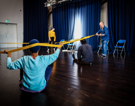 Photo of somar rehearsals - dancers can be seen holding a long stretchy band