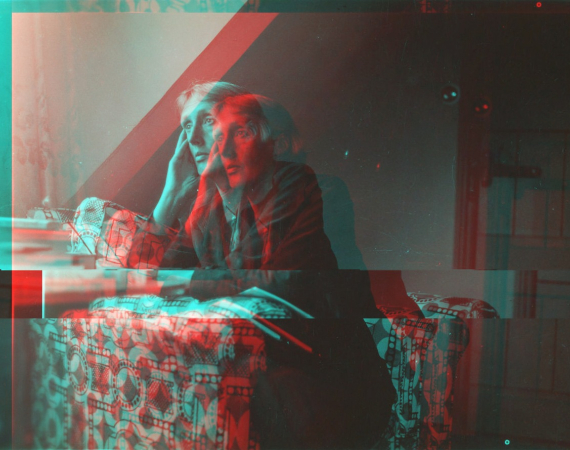A black and white image of a Virgina Wolfe staring, deep in thought out of the window, they sit on an armchair with a bold print. The image glitches and is distorted in red and blue