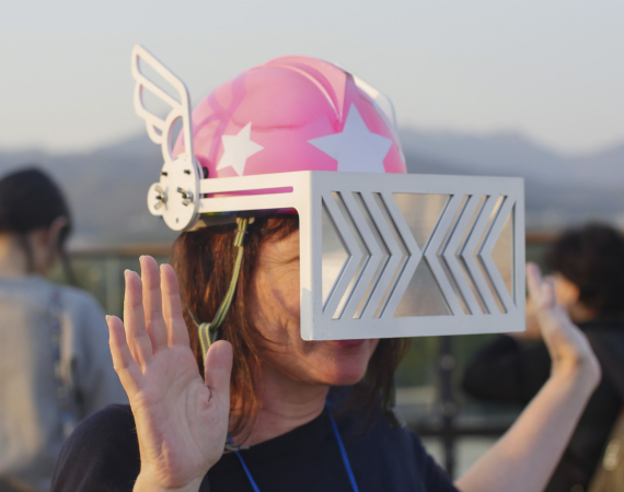 A close up of a person holding their hands up while wearing a pink helmet with silver visor. 