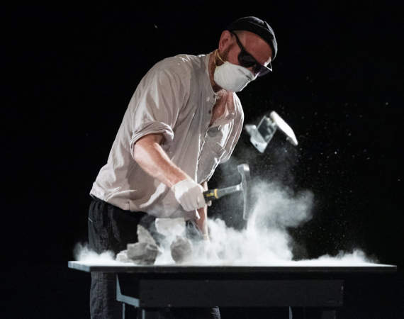 An image of a man smashing rocks in a dark space on a large surface. 