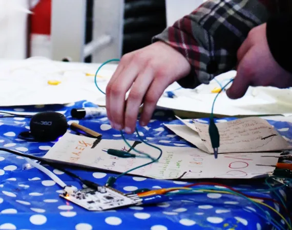 Close up of a pair of hands playing with an Arduino Board with wires coming out of it 