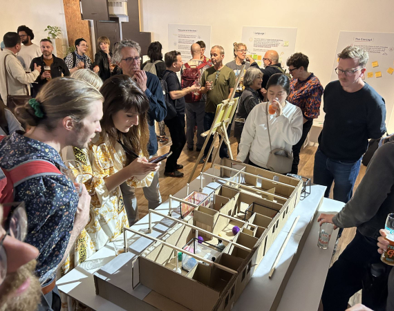 A photo of a group of people looking at a scale model of a building interior and socialising