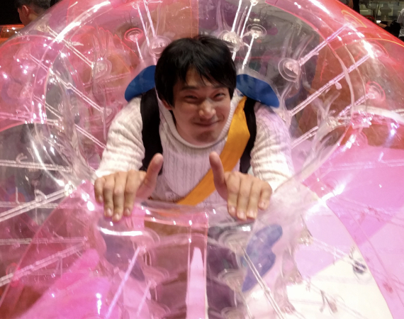 An image of a happy man, smiling at the camera and giving a thumbs up, in a large pink inflatable ring, at the Future Undokai Project. 