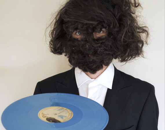Image of Craig Scott with a hairy face holding a blue record.