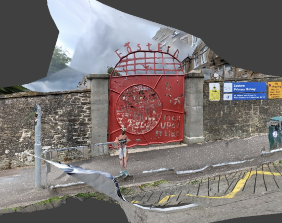 An image of a red gate sidelined by grey walls on either side, by a littered road. 