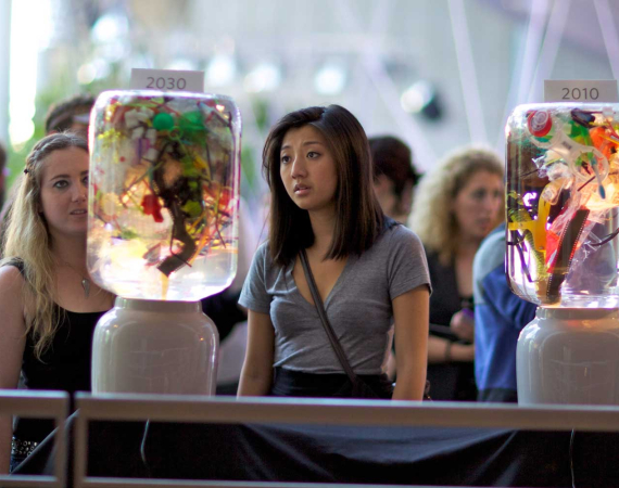 Two women look at an art installation - a collection of diverse plants in a terrarium, situated in a large convention space.