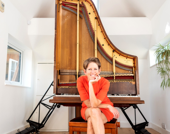 An image of pianist Sarah Nicolls sat in front of her Future Piano, which resembles an open piano positioned on its front.