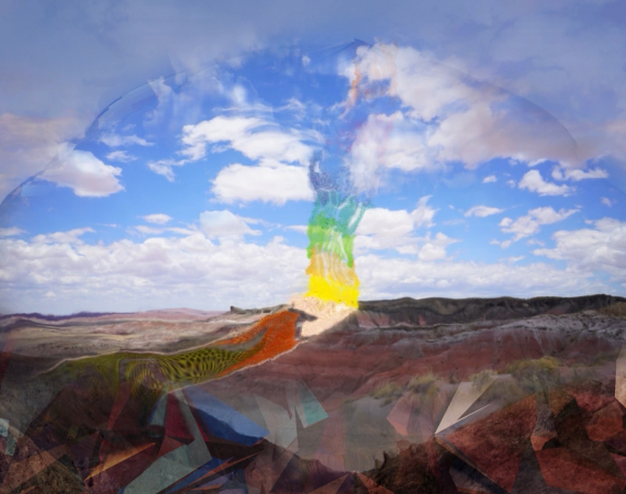 A still from the film I would like to be midnight/I would like to be sky by Amelia Winger-bearskin. The still depicts a landscape, evocative of the deserts of Nevada, beneath a cloudy sky with vibrant blue in between. The center of the image shows a feather like multicoloured implement with barely legible text on it.