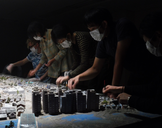 A group of people wearing masks and excavating a model city